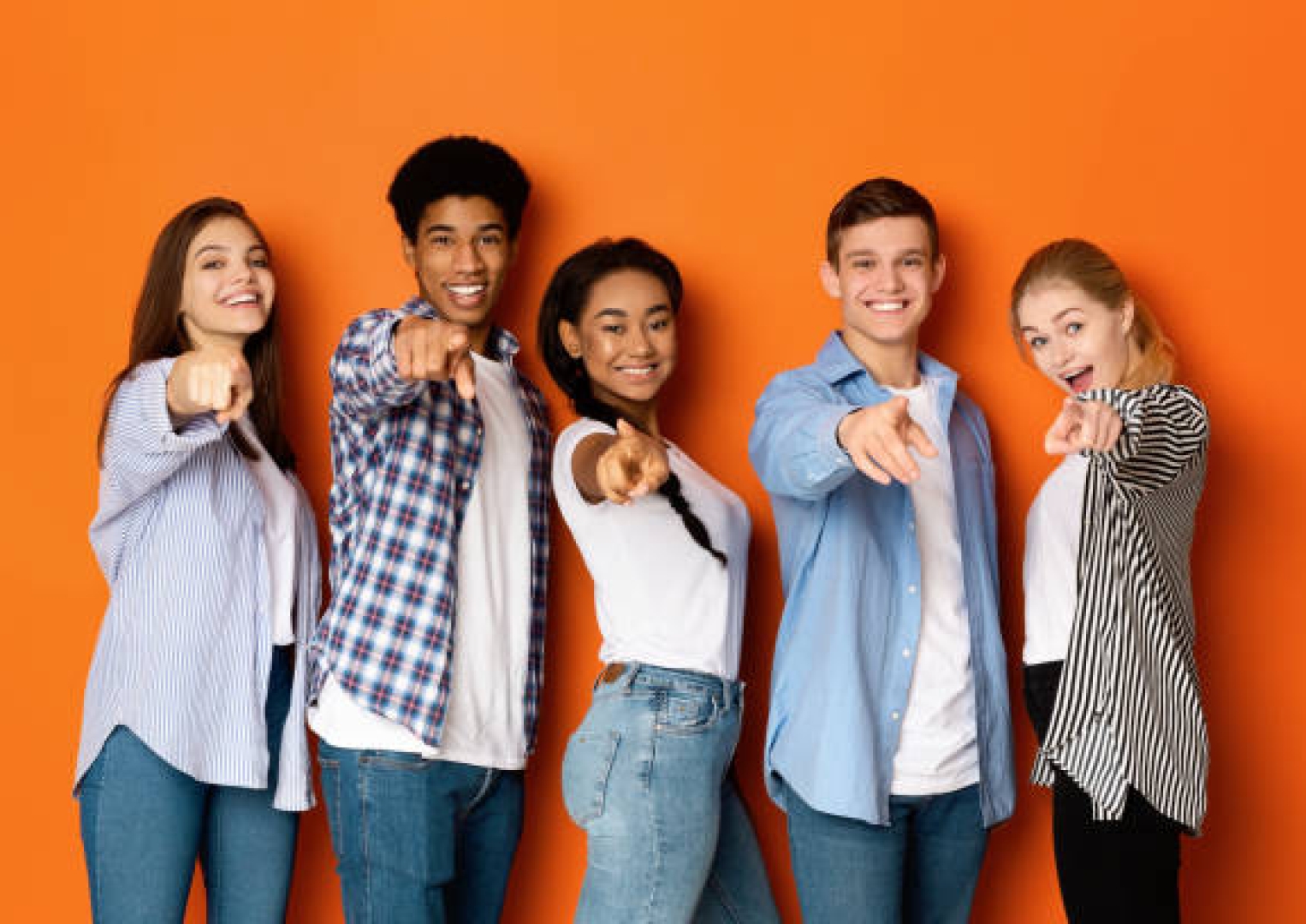 Hey, you! Happy teenagers pointing fingers at camera and smiling over orange background
